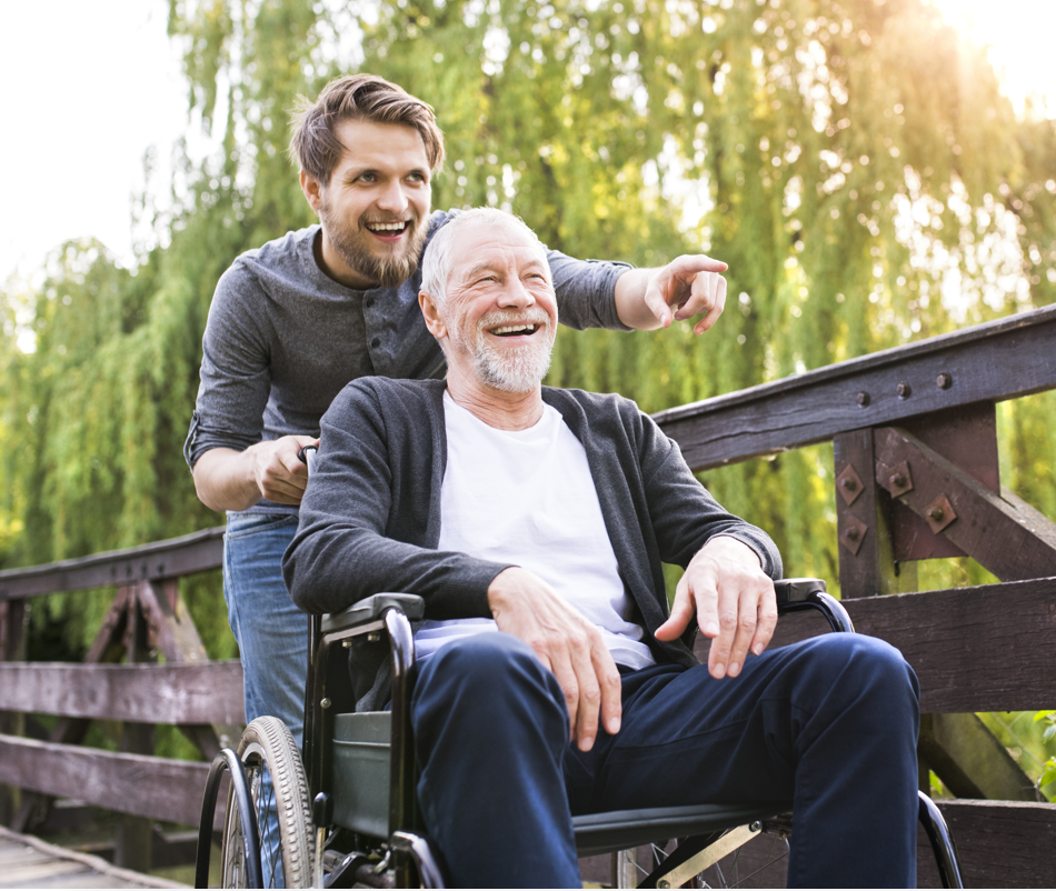 Older man in a wheelchair laughing with man who is pushing him